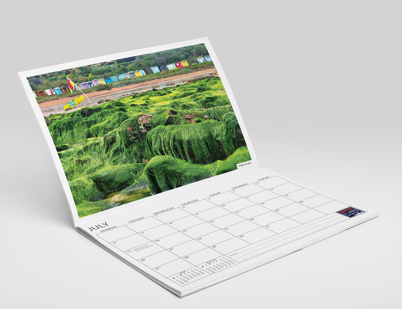 Calendar with view of beach with lichen covered rocks and colourful beach huts